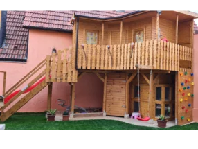 Ein großes Spielhaus aus Holz mit Rutsche und Schaukel.