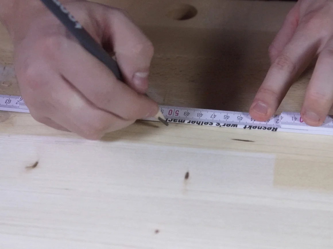 Person markiert Stelle auf Holz mit Bleistift