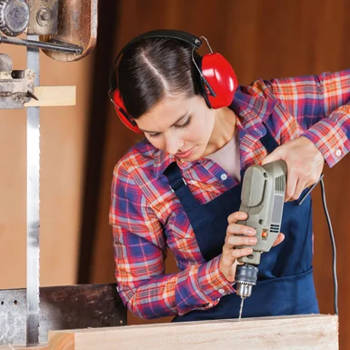 Person mit Gehörschutz bohrt mit Bohrmaschine in Holz