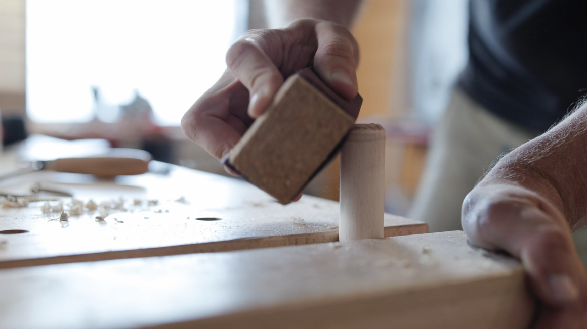 Person schleift Holz mit Schleifpapier.