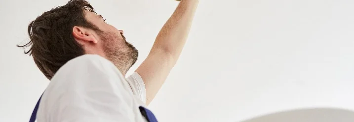 Person befestigt eine Deckenlampe.