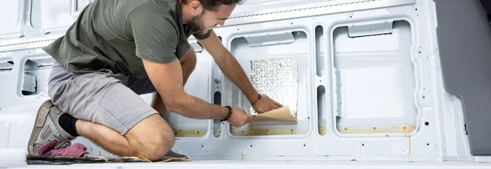 Person beklebt Transporterwand mit Dämmmaterial