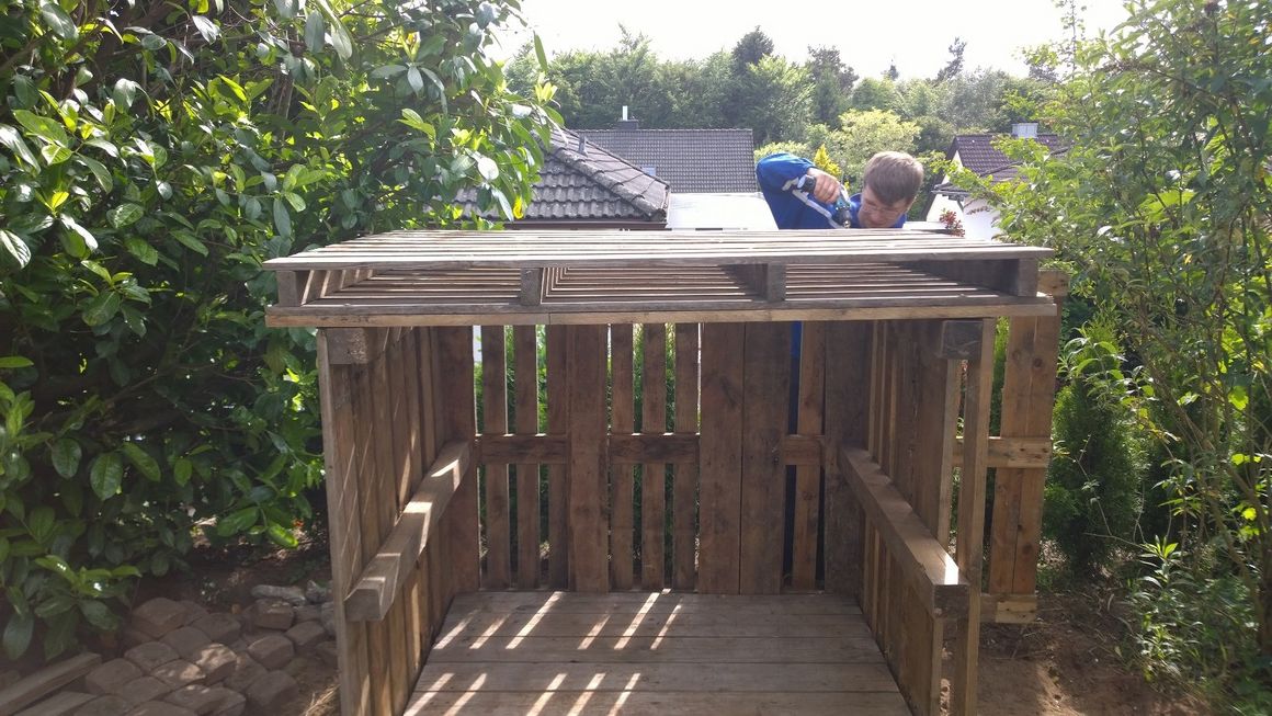Person baut ein Gartenhaus aus Paletten.
