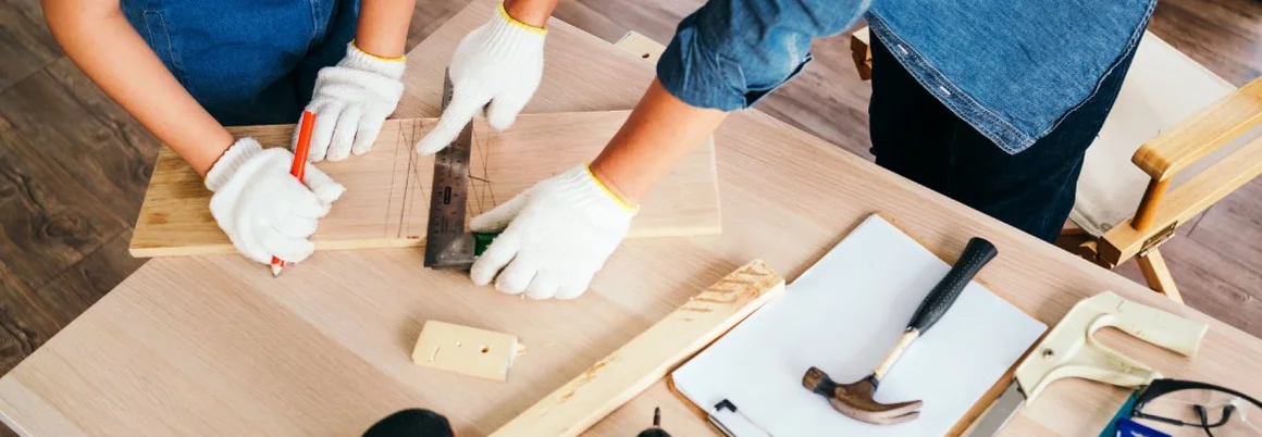 Zwei Personen messen mit einem Winkelmaß ein Holzbrett aus.