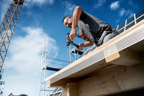 Person baut mit Akkuschrauber an Dachstuhl