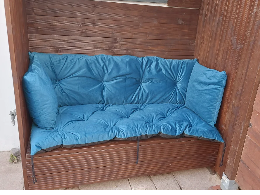 Holzbank mit blauer Sitzauflage in Gartenhütte