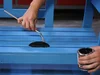 Person streicht Holzbank blau