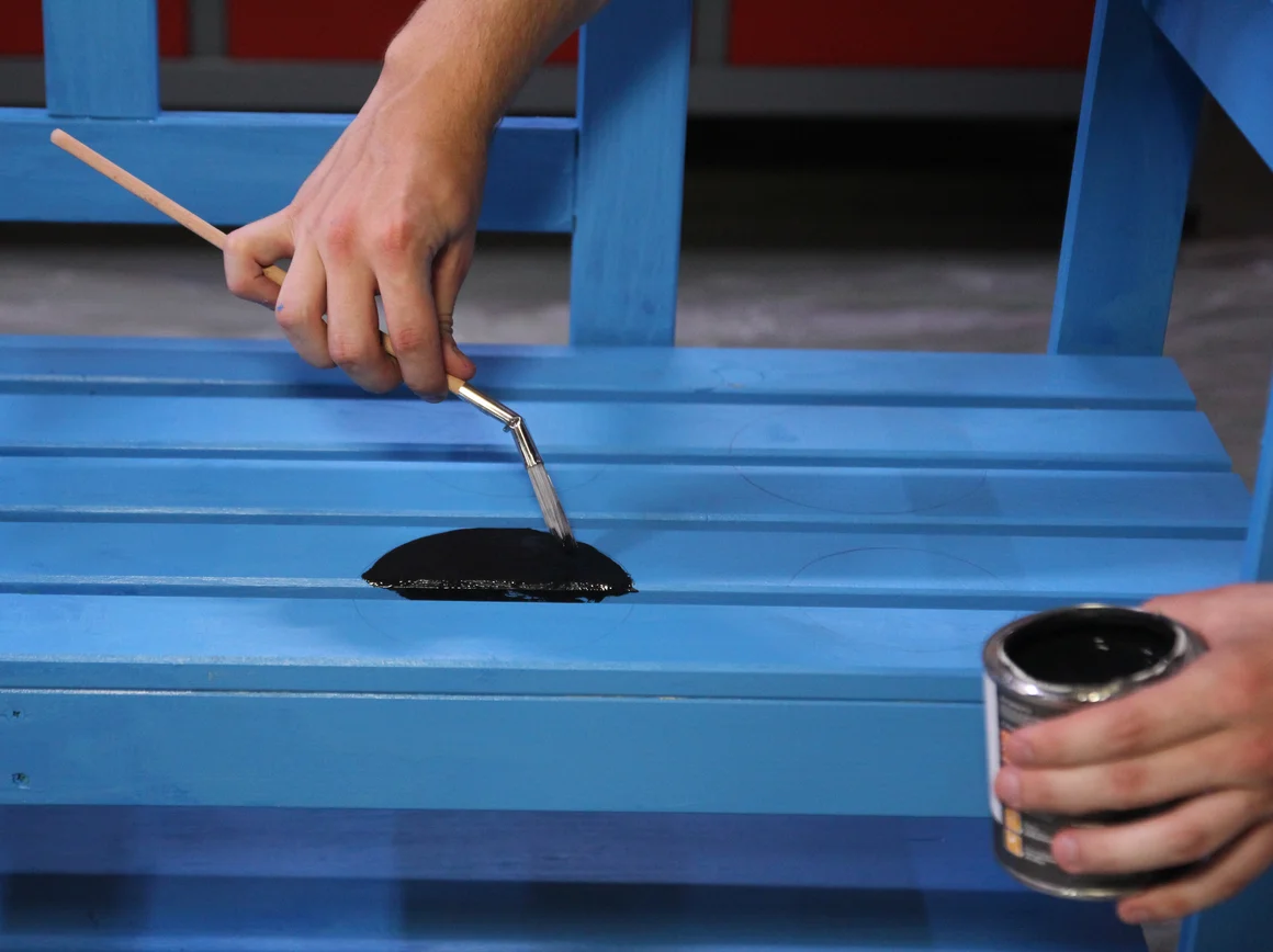Person streicht Holzbank blau