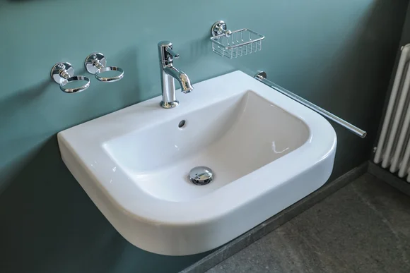 Weißes Waschbecken mit Chromarmaturen an einer grünen Wand