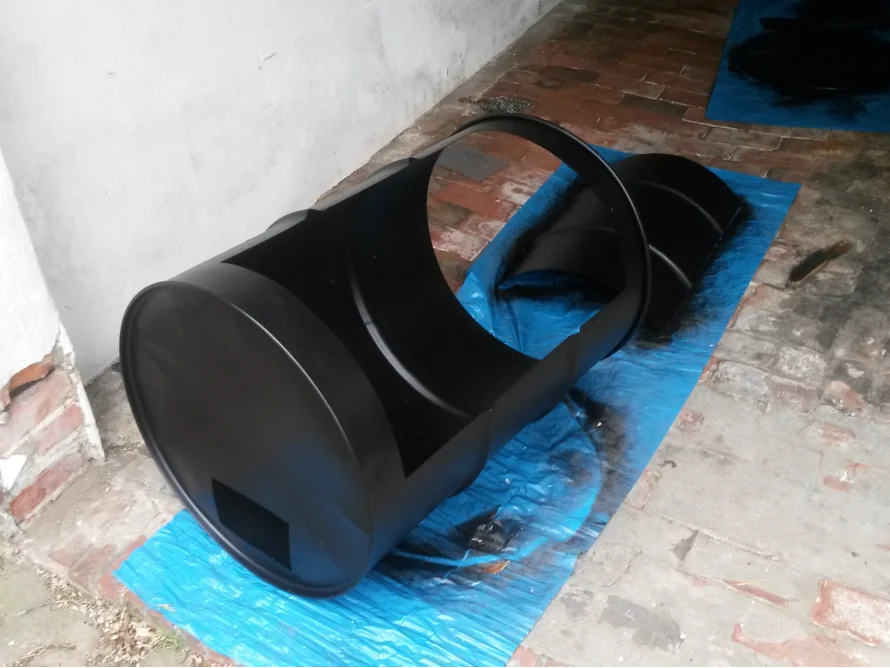 Schwarzes Fass liegt auf blauer Plane.