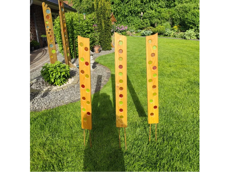 Drei hohe Holzdekorationen mit buntem Glaseinsatz im Garten