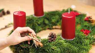 Person dekoriert Adventskranz mit Tannenzapfen
