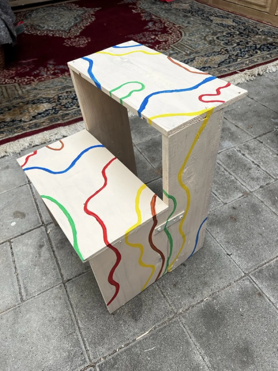 Ein selbstgebauter Tritthocker mit bunten Linien bemalt.