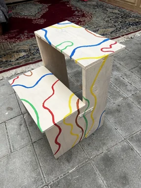 Ein selbstgebauter Tritthocker mit bunten Linien bemalt.