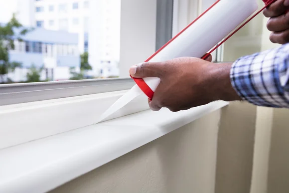 Person versiegelt Fensterrahmen mit Dichtmittel