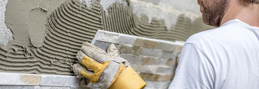Person verlegt Wandfliesen mit Kleber