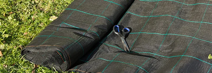 Schwarzes Gartenvlies und Schere auf Rasen
