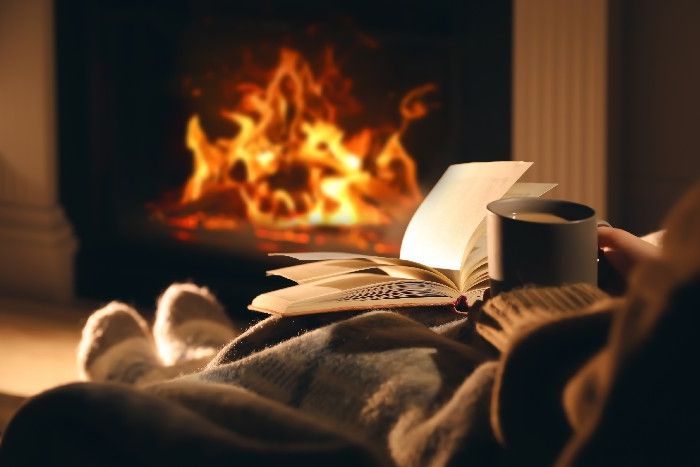 Frau relaxt mit Buch und Tee vor dem Kaminfeuer