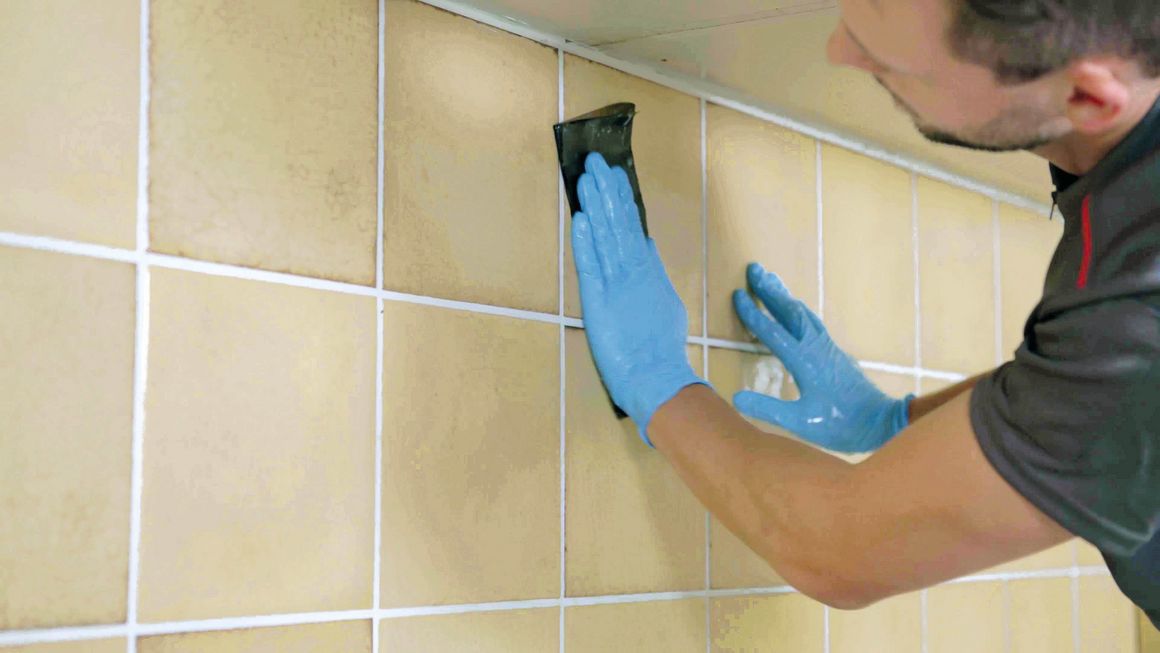 Der Handwerker reinigt die Wandfliesen mit einem Schwammtuch.