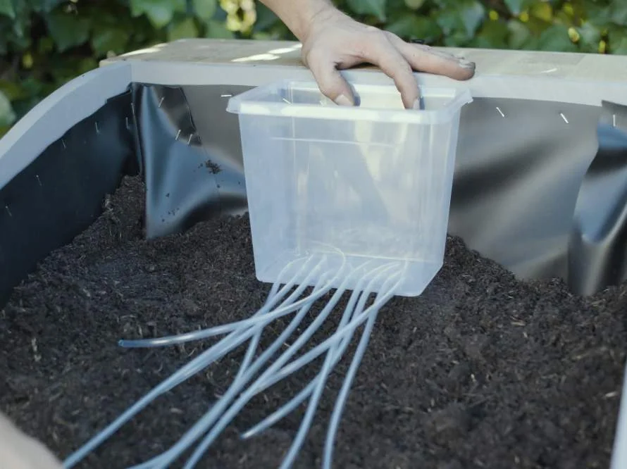 Person platziert einen Kunststoffbehälter in einem Hochbeet.