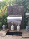 Ein Gartenbrunnen als Wasserfall mit Buddha-Kopf-Dekorationen und einer Holzwand.