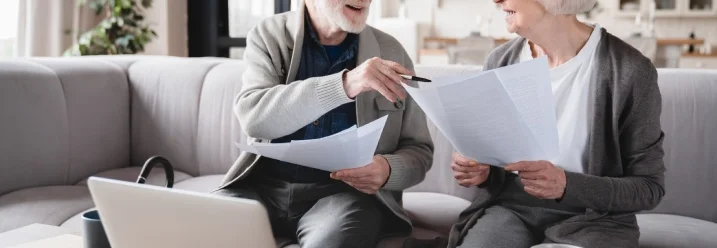Zwei ältere Personen besprechen Unterlagen auf dem Sofa.