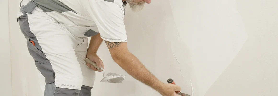 Person verspachtelt Wand mit Spachtel.