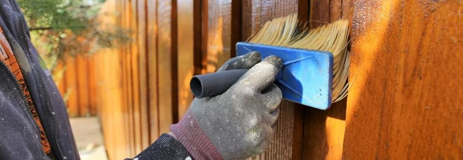 Person streicht Holzzaun mit Pinsel
