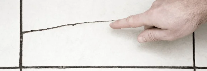 Hand zeigt auf Riss in Fliese