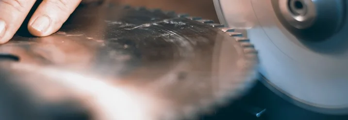 Hand führt Sägeblatt an Schleifscheibe