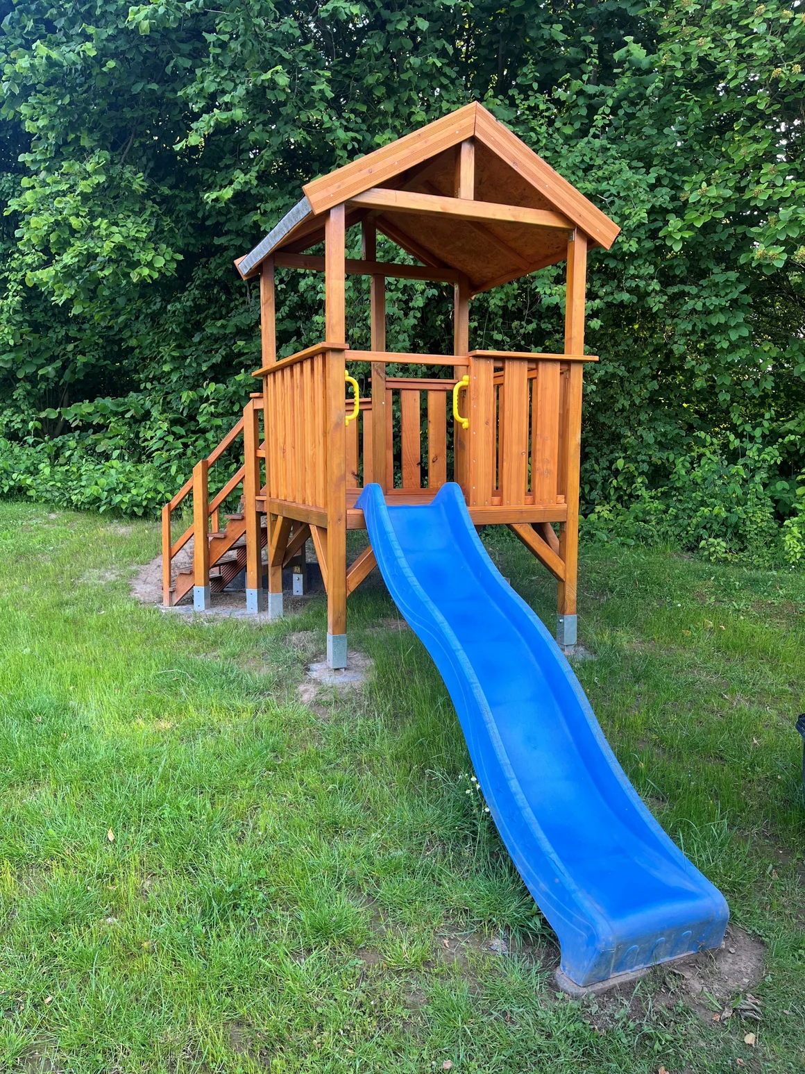 Ein Spielturm aus Holz mit einer blauen Rutsche auf einer Wiese.
