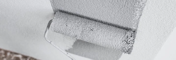 Hand mit Farbrolle trägt graue Farbe auf Wand auf