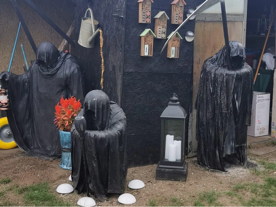 Drei schwarze Gestalten vor Gartenhaus