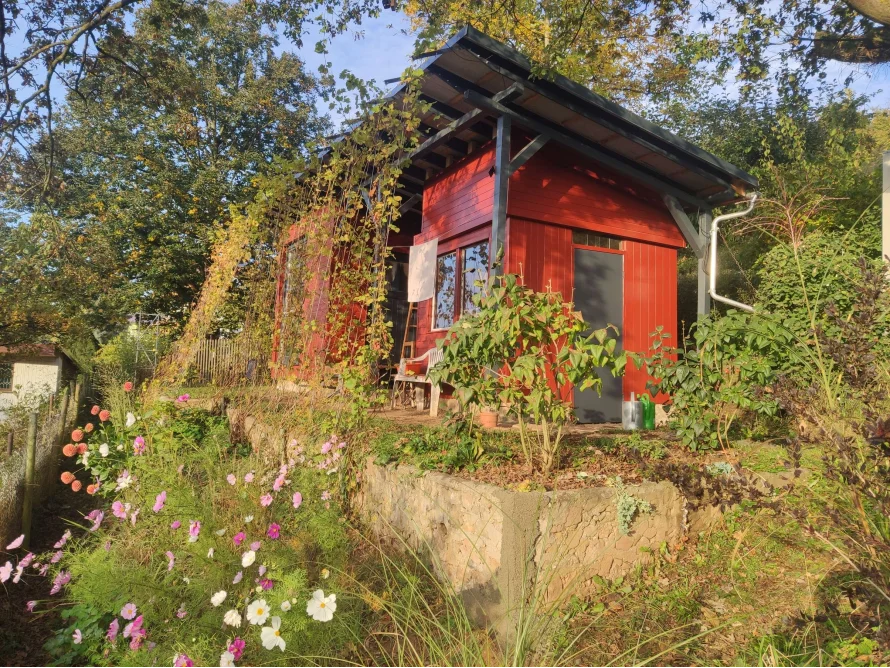 Rotes Gartenhaus, umgeben von Blumen und Pflanzen.
