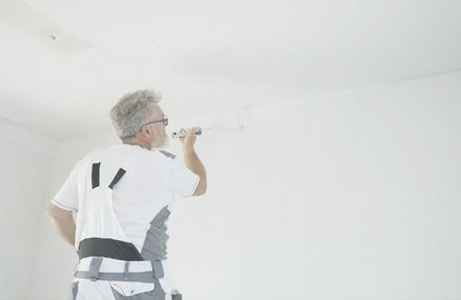 Ein Malermeister streicht die Kante zwischen Zimmerdecke und Wand.
