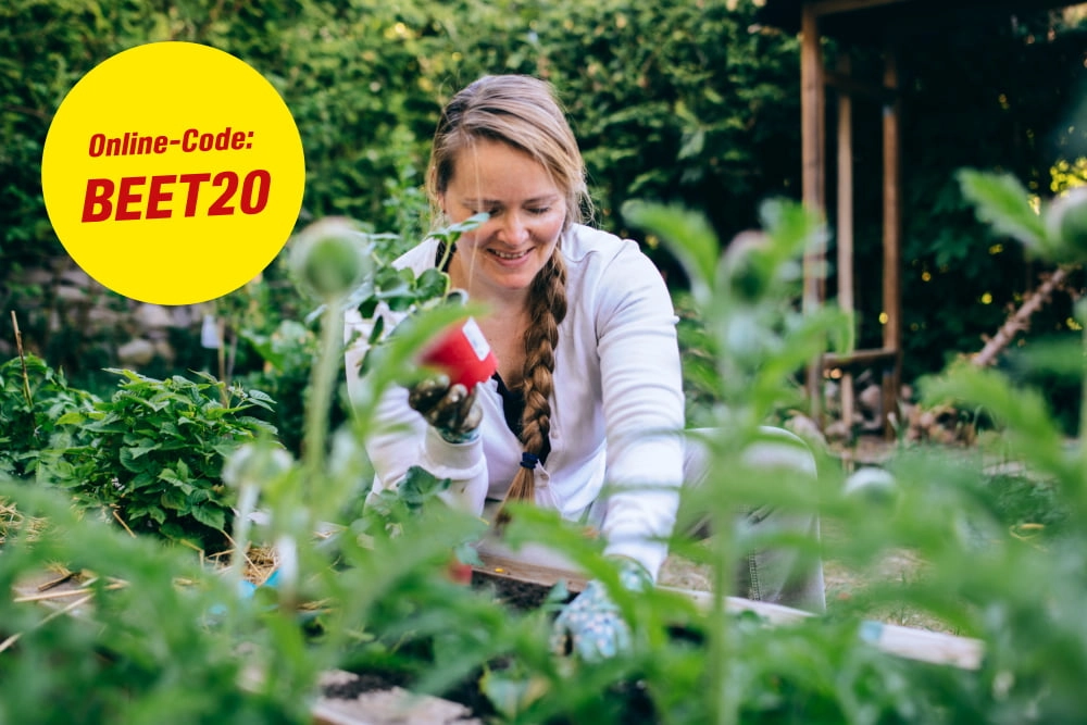 Eine Person pflanzt lächelnd in einem Beet.