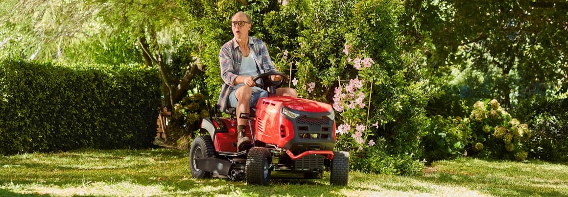 Eine Person mit überraschtem Gesichtsausdruck auf einem roten Rasenmähertraktor.