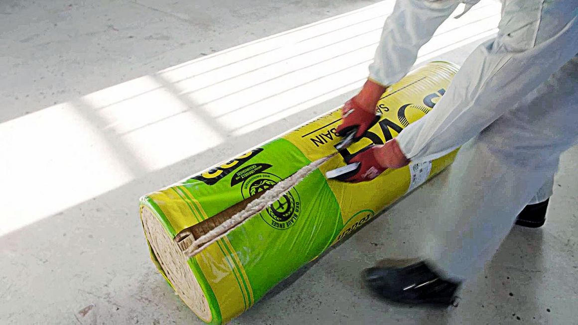 Ein Handwerker schneidet eine Rolle Dämmmaterial auf.