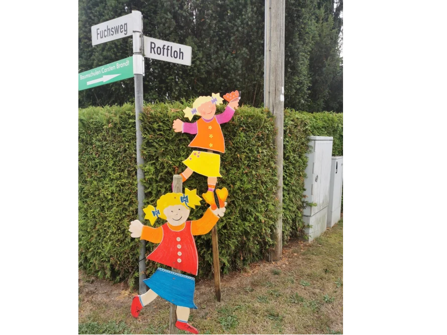 Zwei Kinderfiguren aus Holz an einem Wegweiser
