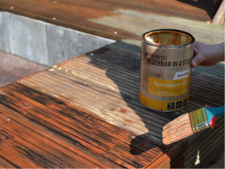 Person ölt Holzterrasse mit Pinsel