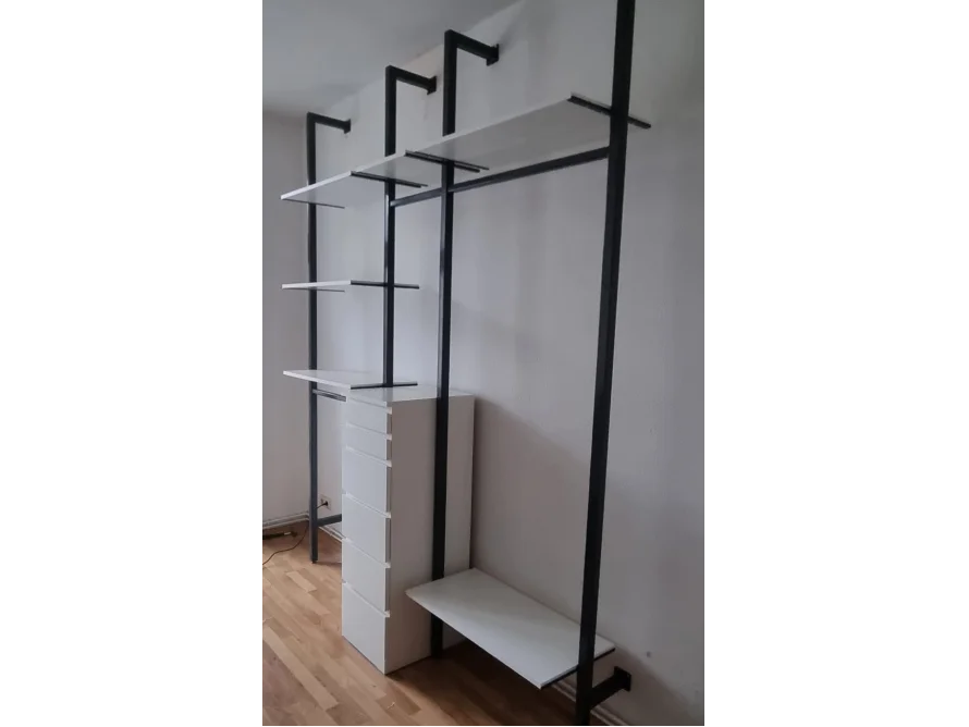 Ein offener Kleiderschrank mit schwarzen Metallrahmen und weißen Regalen und einer Kommode.