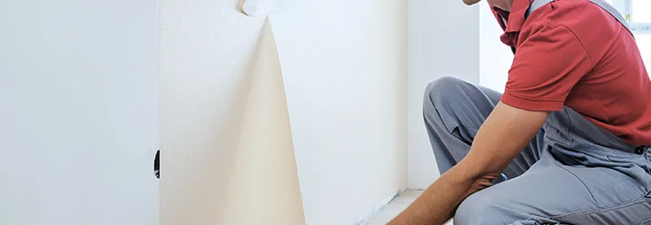 Person entfernt Tapete mit Spachtel.