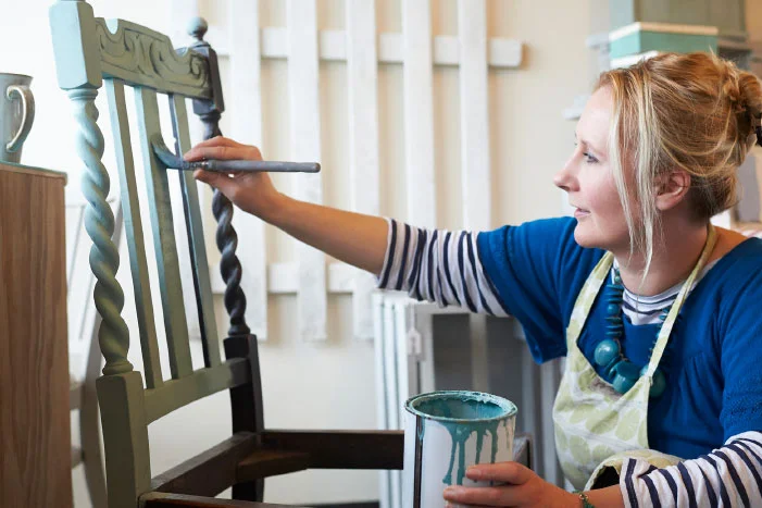 Person streicht Stuhl mit Pinsel