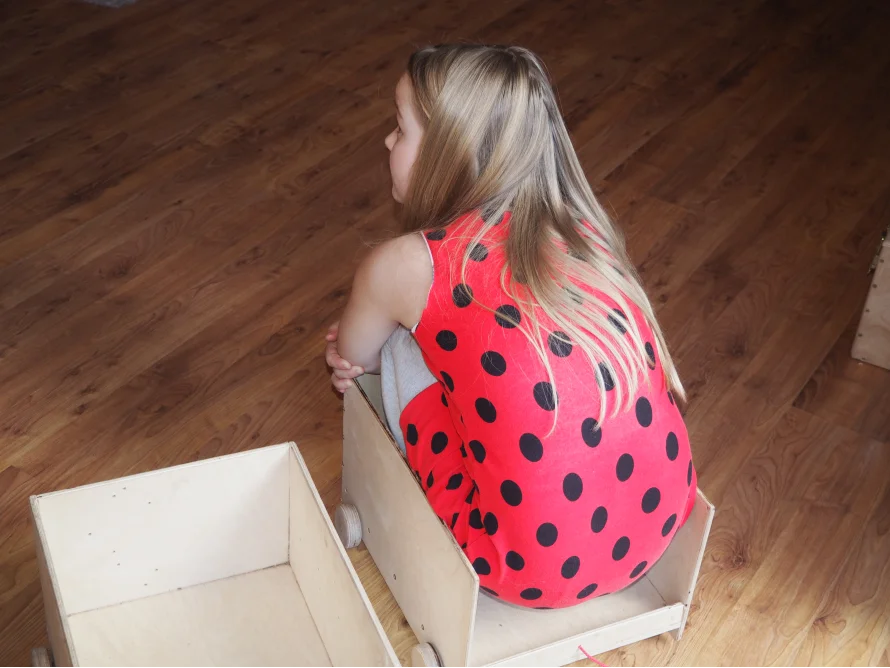 Kind sitzt in einem Spielzeugauto aus Holz