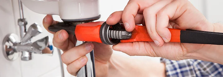 Person repariert ein Waschbecken mit einer Rohrzange.