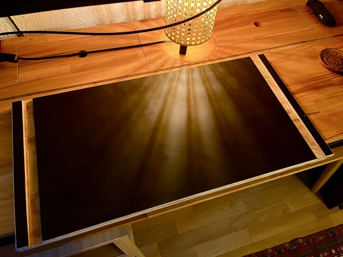 Eine schwarze Schreibtischunterlage auf einem Holztisch, die von einer Lampe beleuchtet wird.