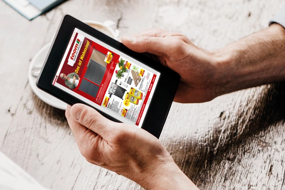 Eine Person hält ein Tablet in den Händen und schaut sich einen Online-Prospekt an.