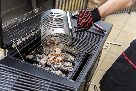 Person schüttet glühende Kohlen in einen Grill