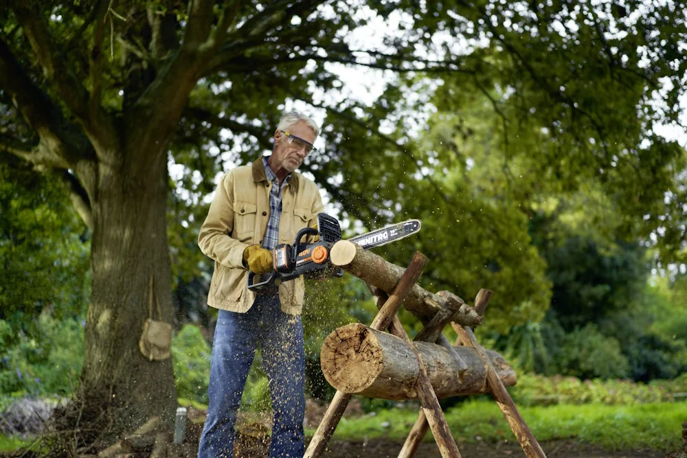 Person sägt mit Kettensäge Baumstamm.