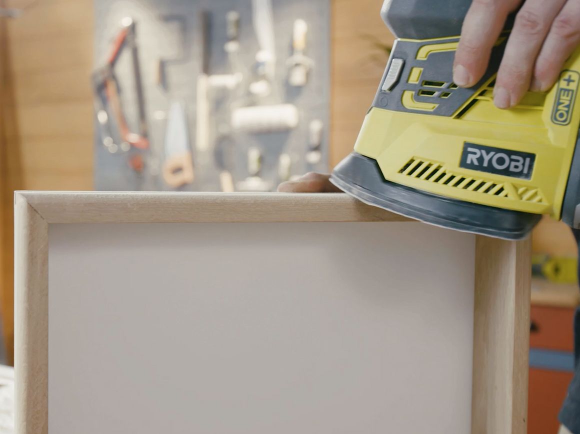 Person schleift Holzrahmen mit Schleifmaschine